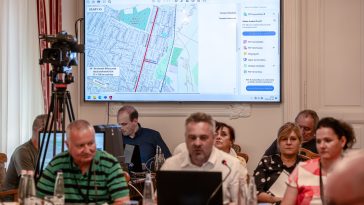 A Dózsa György és az Arany János utcák terve a kivetítőn, Moldován Attila tervező az előtérben a 2025. augusztus 28-i testületi ülésen.
