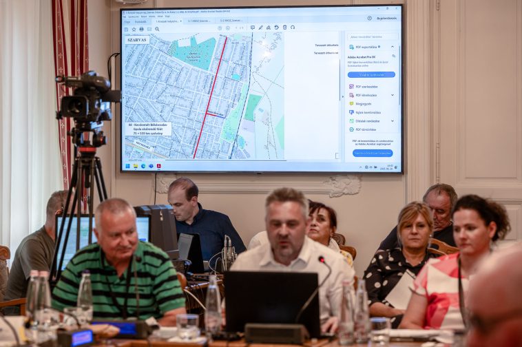 A Dózsa György és az Arany János utcák terve a kivetítőn, Moldován Attila tervező az előtérben a 2025. augusztus 28-i testületi ülésen.